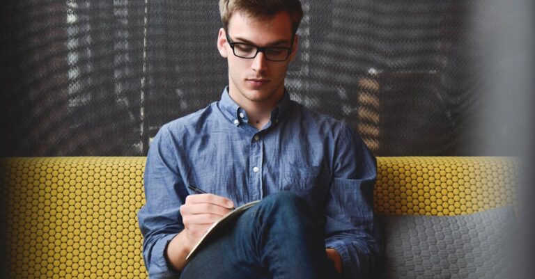 Person in Blue Denim Jacket Sitting on Chair While Writing