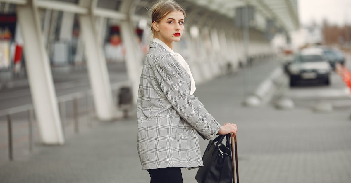 Stylish young woman with suitcase near car parking in airport