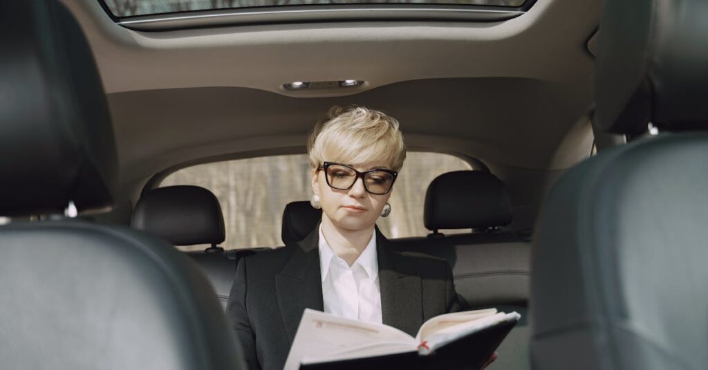 From below of concentrated female entrepreneur in elegant formal clothes sitting on backseat while reading memos in notebook riding in car