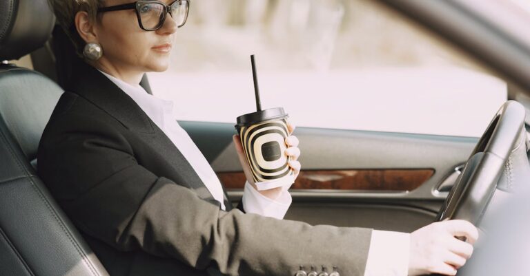 Stylish woman with takeaway coffee driving car