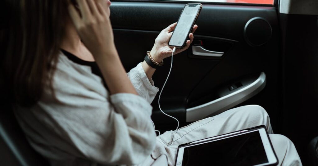 From above side view of crop anonymous female worker sitting in car with tablet and cellphone with blank screen while using earphones