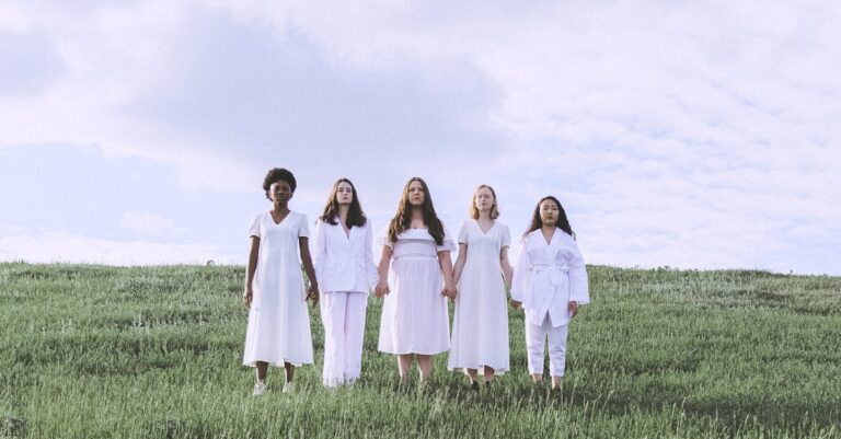 Women Holding Hands While Standing on Green Grass Field Under White Clouds