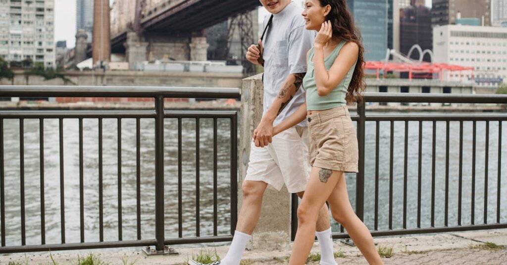 Stylish diverse couple holding hands and strolling on city promenade under bridge over river