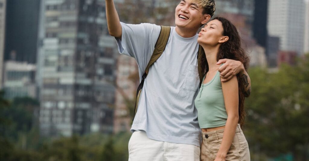 Full body of positive young diverse couple in stylish clothes hugging and taking selfie on mobile phone while spending holidays in New York City