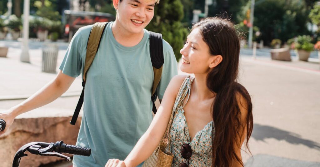 Cheerful multiracial couple in casual clothes walking with bicycles on city street in daylight