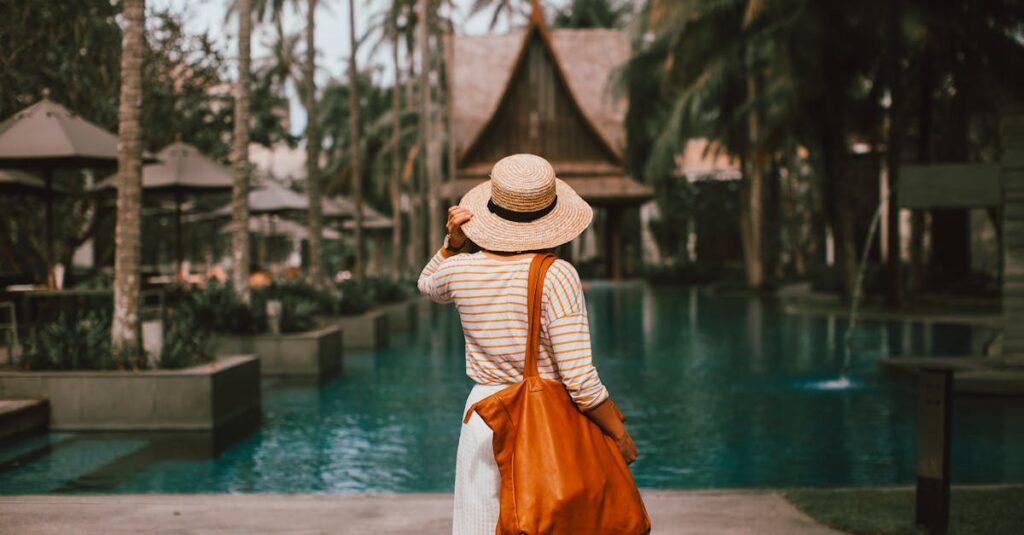 Unrecognizable woman in hat standing on poolside in resort