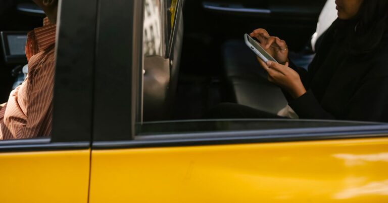 Side view of unrecognizable passenger browsing smartphone while sitting on backseat of yellow cab with anonymous driver during ride