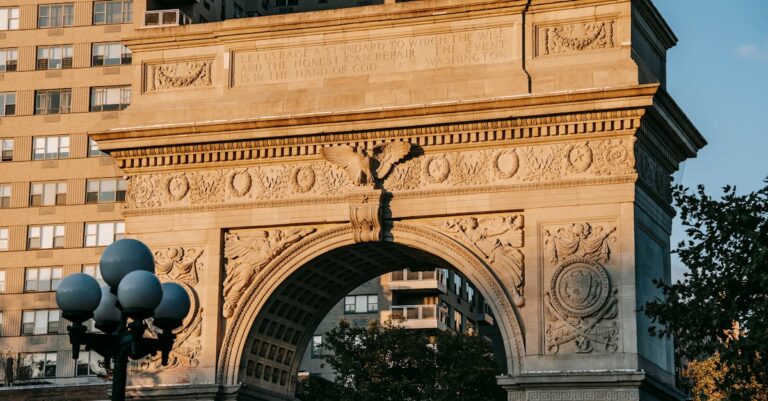 From below of aged triumphal arch placed in Washington Square Park in New York City against residential building illuminated by sunlight