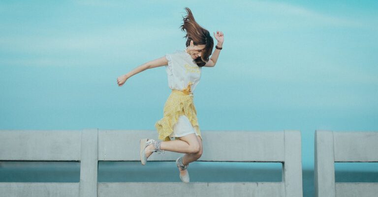 Jumpshot Photography of Woman in White and Yellow Dress Near Body of Water