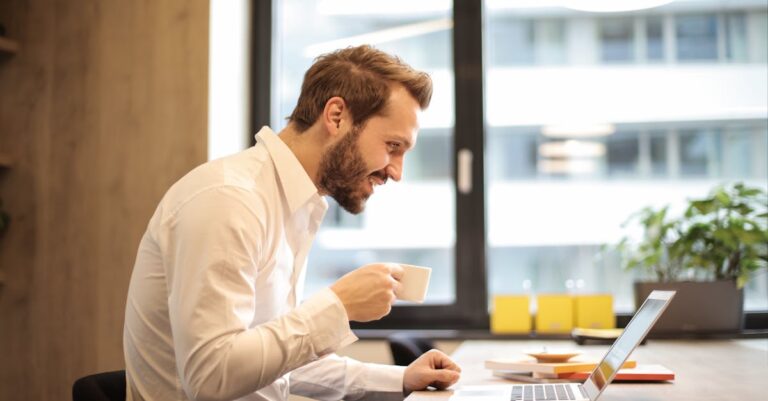 Man Holding Teacup Infront of Laptop on Top of Table Inside the Room