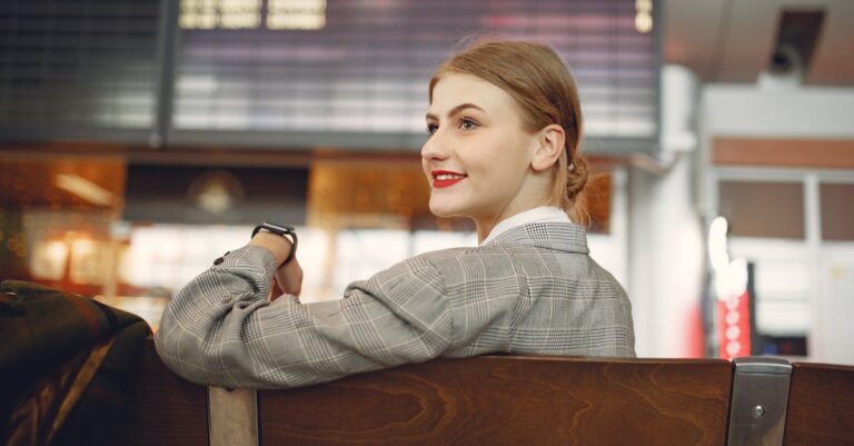 Side view of positive female manager waiting for flight on wooden seat in airport