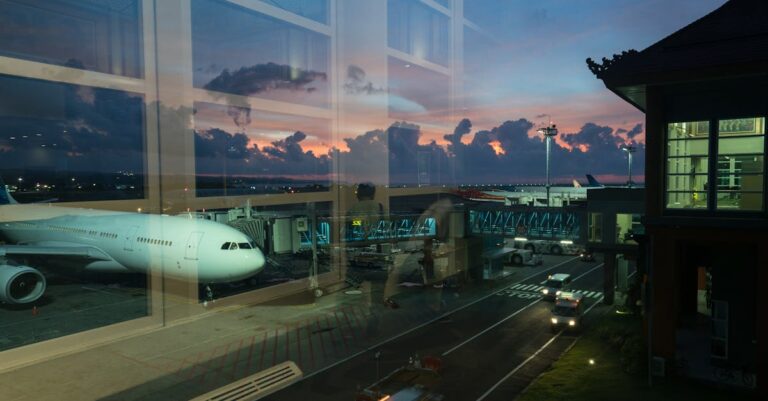 Through glass modern aircraft parked near airbridge in contemporary airport against picturesque dusk sky