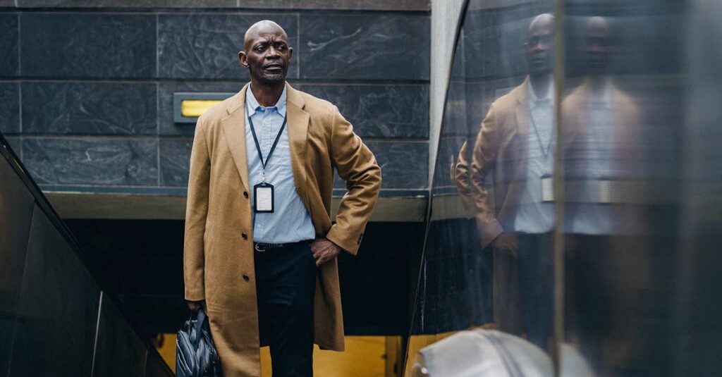 Confident adult African American businessman in formal clothes riding escalator with hand in pocket while leaving metro station and looking away thoughtfully