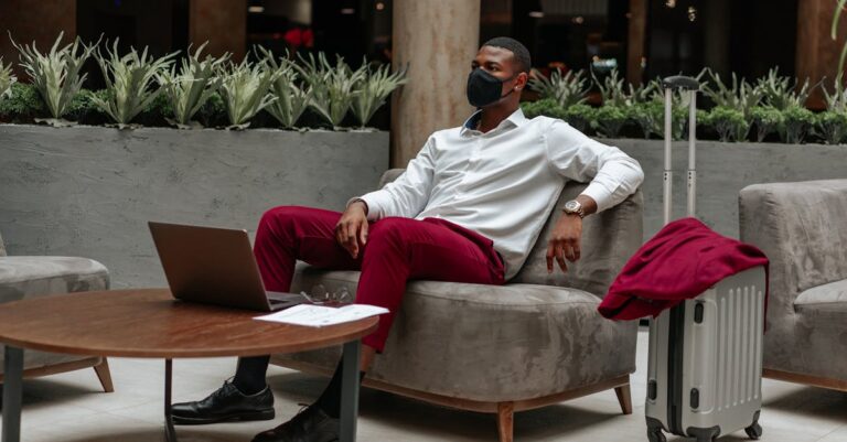 Man in White Long Sleeves and Maroon Pants Sitting on Sofa In Front of a Laptop