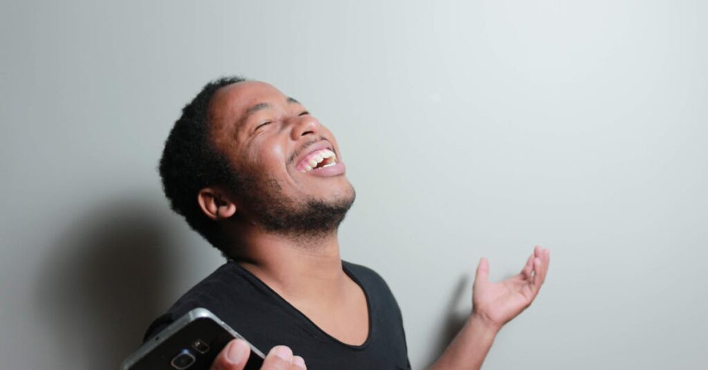 A cheerful man joyfully expresses happiness while holding a smartphone indoors.