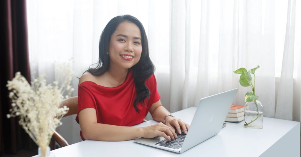 Smiling businesswoman in red dress working on laptop at a modern office desk.