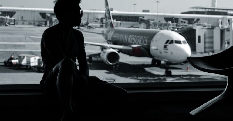 A silhouetted man sits in an airport terminal, viewing an airplane on the tarmac.