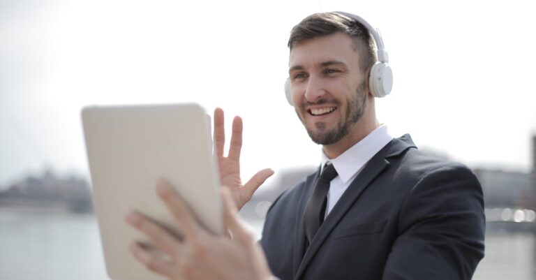 Smiling businessman in suit using a tablet with headphones outdoors, engaging in a video call.