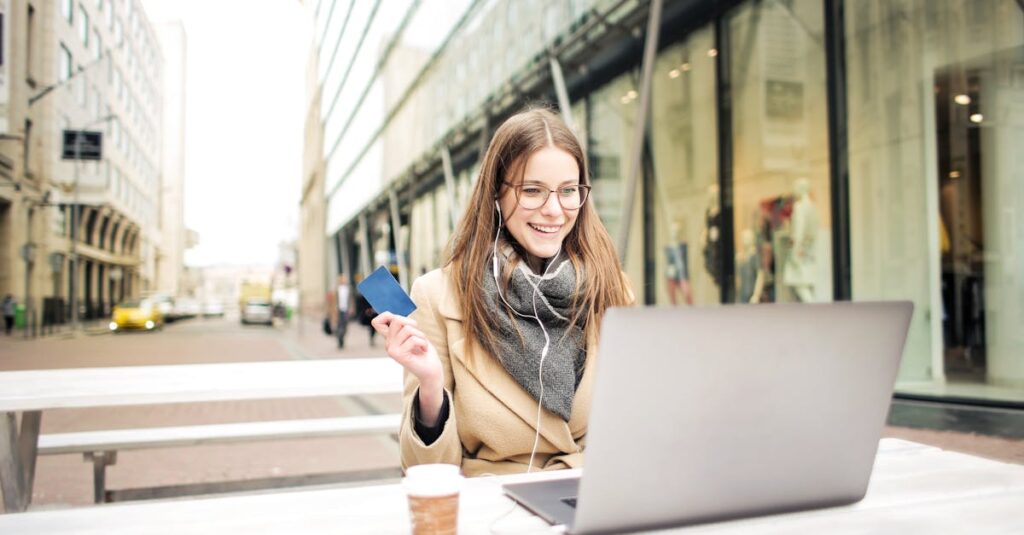 Businesswoman smiling while using laptop and holding credit card outdoors.