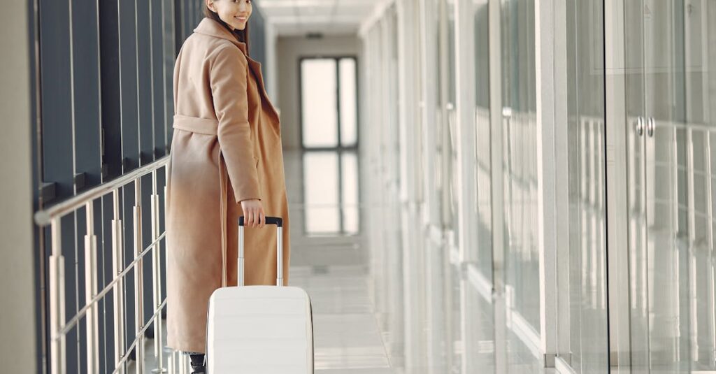 A cheerful woman in a stylish coat walks through an airport terminal with her suitcase.