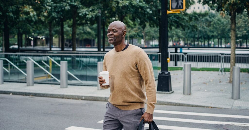 Mature African American man carrying disposable coffee cup and personal bag crossing street in downtown