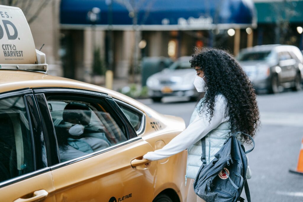 Side view of unrecognizable African American lady with long dark hair in casual clothes and medical mask opening door of ta parked on city street