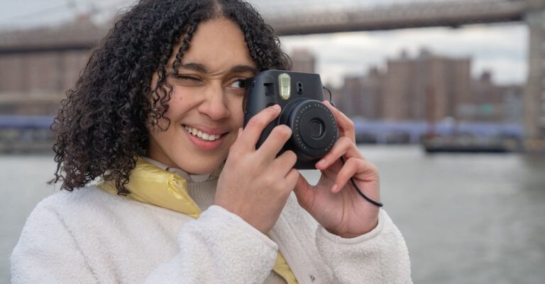 Young woman taking photos near a city bridge with a camera, capturing urban scenes.