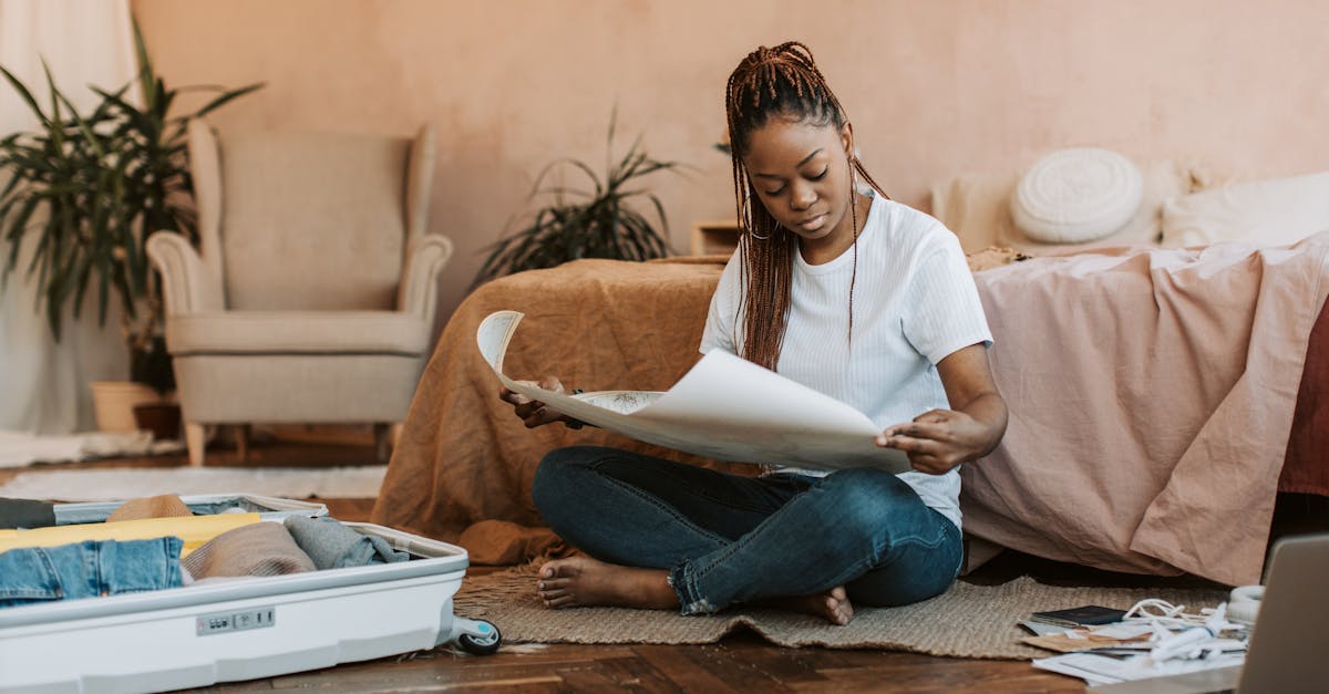 Woman with dreadlocks sitting in bedroom folding clothes into suitcase, preparing for travel.