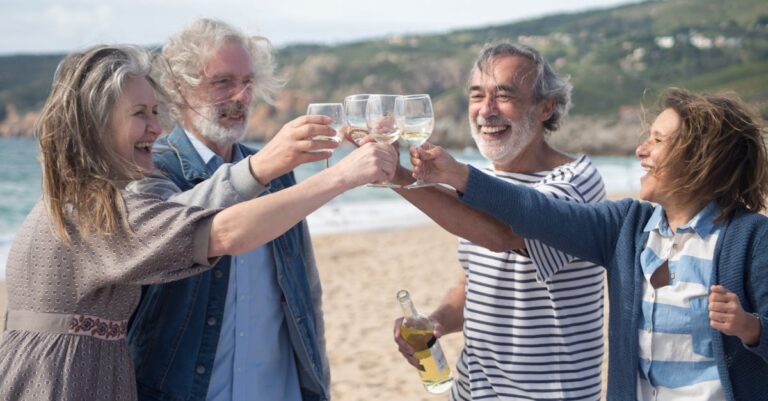 Elderly friends celebrating with wine on a sunny Portuguese beach, embracing happiness and togetherness.