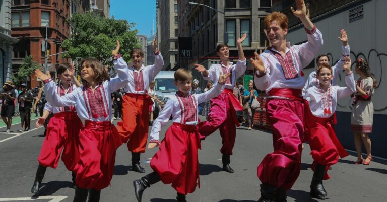 Group of dancers in traditional attire performing on a street in New York City during a summer festival.