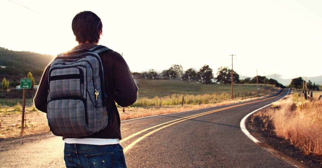 A traveler with a backpack walks on a winding road in the countryside during sunset, symbolizing adventure and freedom.