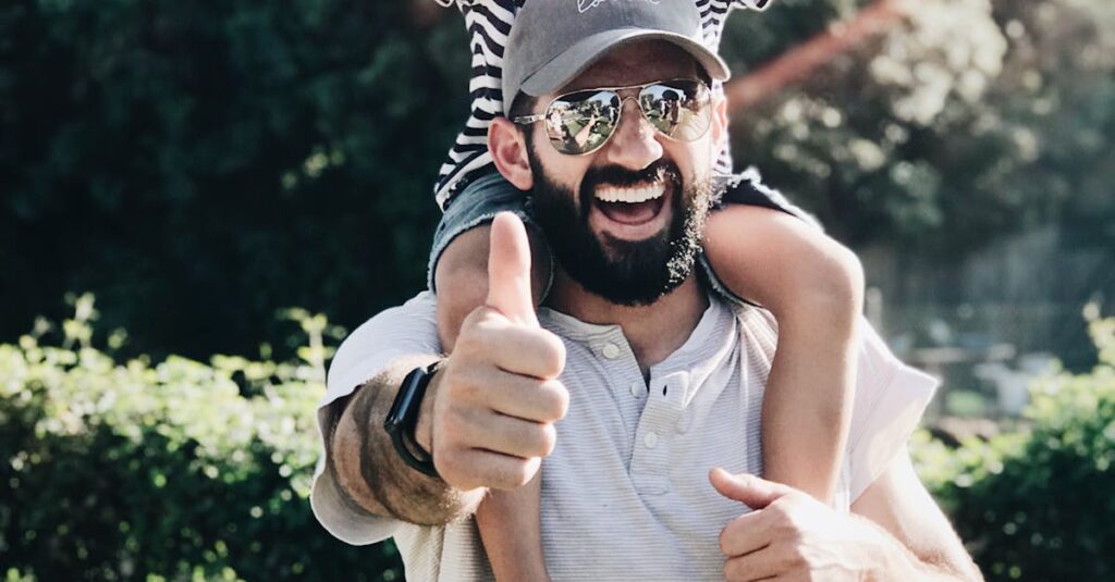 Father giving son a ride on shoulders, both laughing and smiling in a park setting.