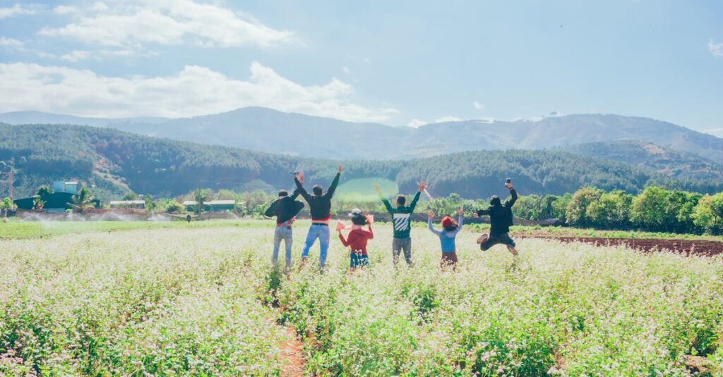 A group of people jumping with joy in a beautiful countryside field surrounded by mountains and clear skies.