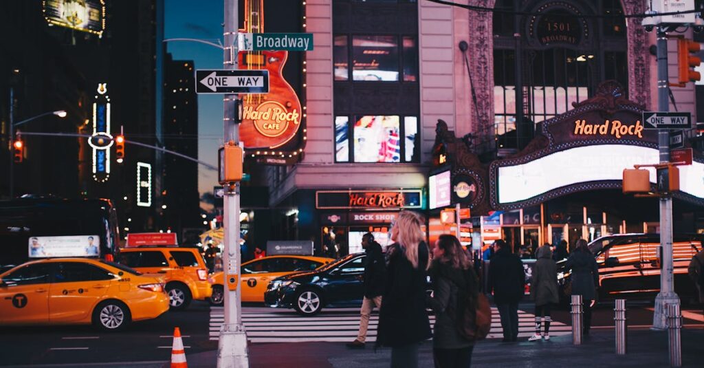 A bustling street view of Broadway at night featuring Hard Rock Cafe, taxis, and pedestrians in New York City.