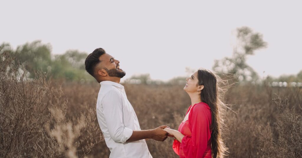 Joyful couple holding hands and laughing in a sunlit summer field.