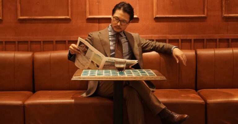 A well-dressed man in a suit reads a newspaper while seated in a chic café.