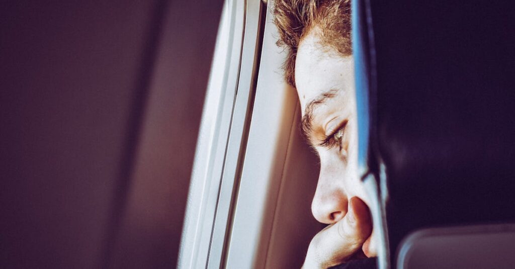 A young man looks thoughtfully out of an airplane window, captured in a close-up portrait.