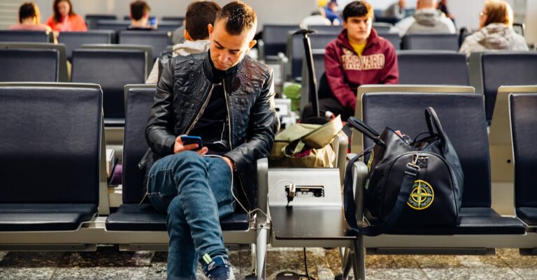 People sitting in an airport lounge, focused on smartphones and waiting for flights.