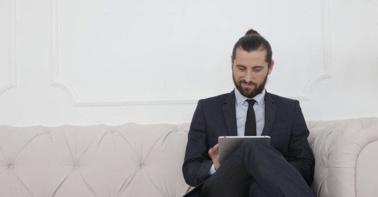 A businessman in a suit sitting on a sofa using a tablet, smiling.