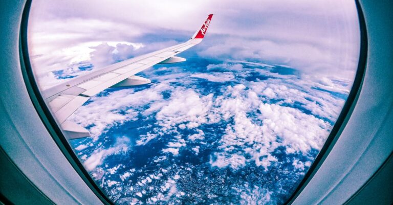 Wide angle of rocky ground through cloudy sky and plane wing from window of aircraft