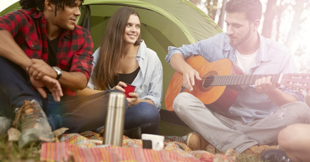 A group of young friends enjoying a summer camping trip with music and relaxation outdoors.