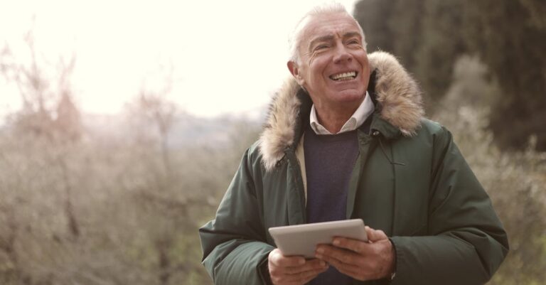 Happy senior man in winter coat enjoying a day outdoors with a tablet.