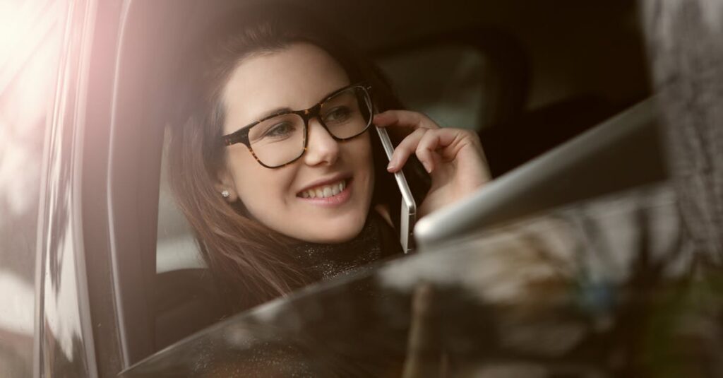 A smiling woman talking on her smartphone inside a car, enjoying a pleasant conversation.