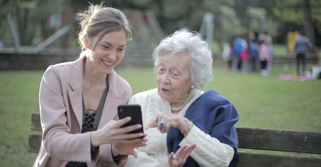 Delighted female relatives sitting together on wooden bench in park and browsing mobile phone while learning using