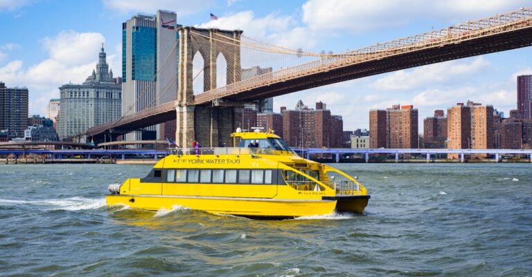 New York Water Taxi sails near Brooklyn Bridge against the NYC skyline on a sunny day.