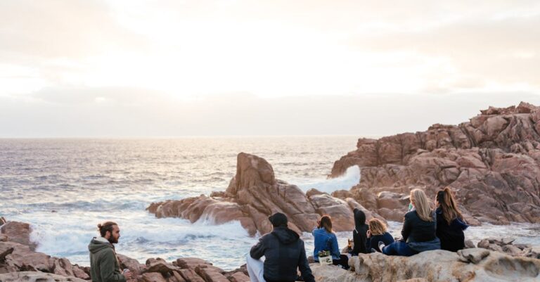 Friends relax on a rocky coast, enjoying the ocean view at sunset.