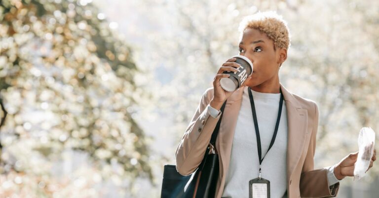 A confident businesswoman enjoys a coffee break outdoors on a sunny day.