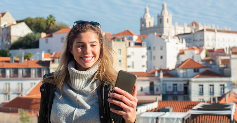 A young woman smiles as she takes a selfie in Lisbon's historic Alfama district on a sunny day.