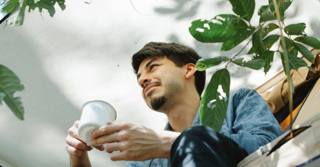 Young man with dark hair relaxing with coffee in a tranquil outdoor campsite.