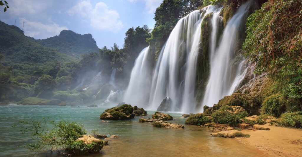 Majestic view of Ban Gioc Waterfall cascading into a serene pool amidst lush greenery in Cao Bang, Vietnam.